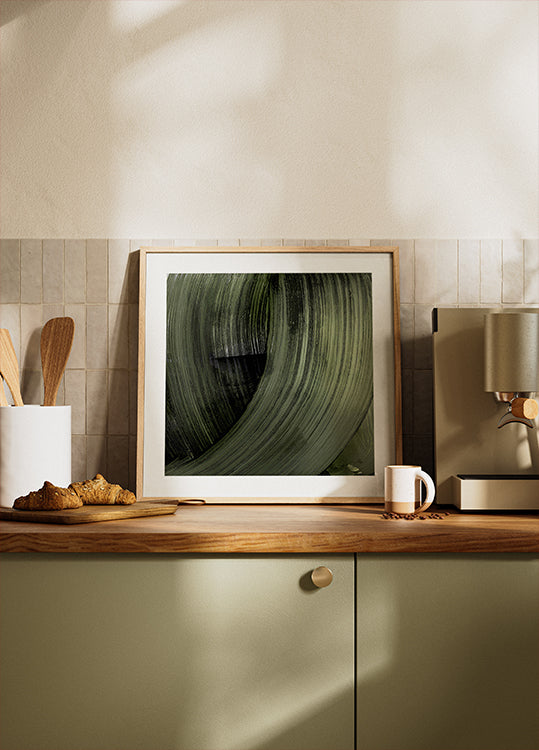 ein gerahmtes Foto eines grünen Blattes auf einer Küchentheke, im Hintergrund sind eine Kaffeemaschine und andere Küchenutensilien zu sehen.